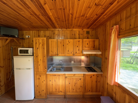 Wooden kitchen in Chalet Bois at Huttopia Barcelona Pirineos in Spain, featuring fridge, stove, and window.