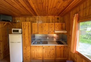 Cucina in legno al Chalet Bois presso Huttopia Barcelona Pirineos in Spagna con frigo, fornello e finestra.