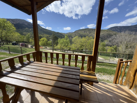 Vista desde el porche de madera en Chalet Bois, con montañas, árboles verdes y cielo parcialmente nublado.