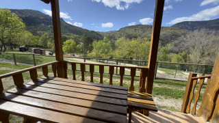 Vista desde el porche de madera en Chalet Bois, con montañas, árboles verdes y cielo parcialmente nublado.
