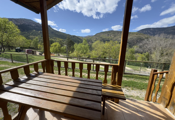 Vista desde el porche de madera en Chalet Bois, con montañas, árboles verdes y cielo parcialmente nublado.