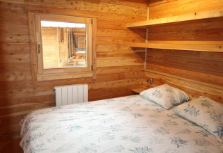 Soveværelse i træ med dobbeltseng og hylder på Montana Chalet Vista, Huttopia Barcelona Pirineos i Spanien.