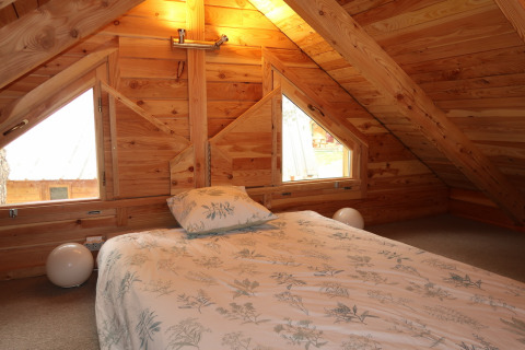 Cozy attic bedroom with wooden walls, bed, and pillows at Montana Chalet Vista, Huttopia Barcelona Pirineos, Spain.