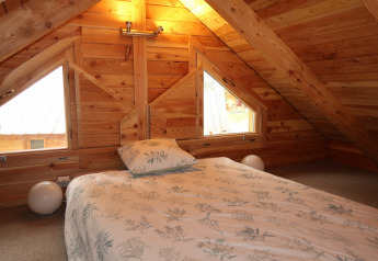 Cozy attic bedroom with wooden walls, bed, and pillows at Montana Chalet Vista, Huttopia Barcelona Pirineos, Spain.