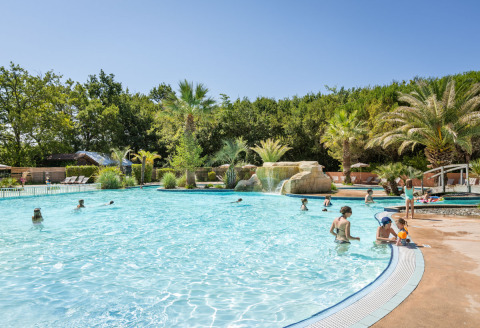 Family enjoying an outdoor pool surrounded by palm trees at Huttopia Lac d'Aureilhan - Mimizan holiday park.