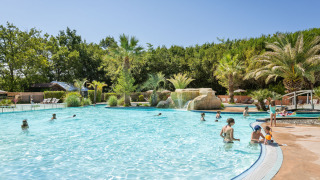 Family enjoying an outdoor pool surrounded by palm trees at Huttopia Lac d'Aureilhan - Mimizan holiday park.
