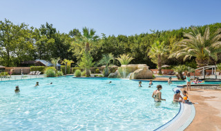 Family enjoying an outdoor pool surrounded by palm trees at Huttopia Lac d'Aureilhan - Mimizan holiday park.