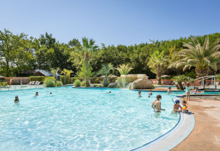 Family enjoying an outdoor pool surrounded by palm trees at Huttopia Lac d'Aureilhan - Mimizan holiday park.