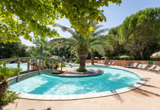 Piscina con isola di palme e ponticello al parco vacanze Huttopia Lac d'Aureilhan - Mimizan in Francia.