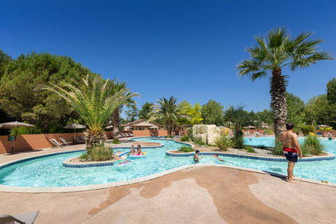 Families enjoy swimming and relaxing by a palm-lined outdoor pool at Huttopia Lac d'Aureilhan, Nouvelle-Aquitaine.