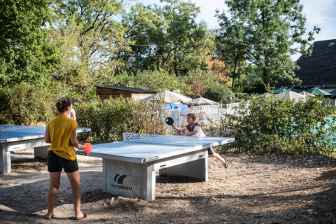 Dos personas juegan tenis de mesa al aire libre en Huttopia Lac d'Aureilhan - Mimizan, un parque vacacional en Francia.