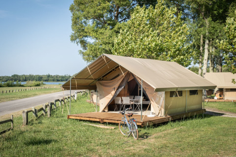 Tente safari appelée Classic Tent avec terrasse en bois et vélo, dans un cadre verdoyant et paisible.