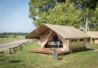 Safari-Zelt namens Classic Tent mit Holzterrasse und Fahrrad, gelegen in grüner, naturnaher Umgebung.
