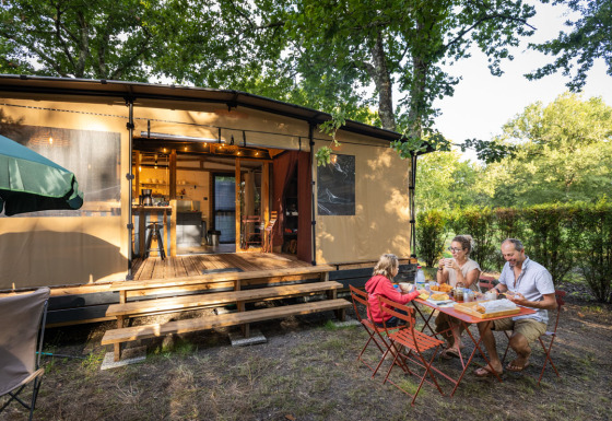 Famille prenant un repas en plein air devant la tente safari Arizona à Huttopia Lac d'Aureilhan - Mimizan, France.