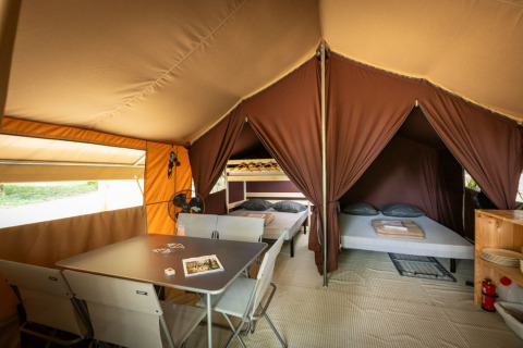 Vista interna di una tenda safari classica con tavolo da pranzo, sedie e due zone notte a Huttopia Lac d'Aureilhan.