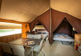 Vista interna di una tenda safari classica con tavolo da pranzo, sedie e due zone notte a Huttopia Lac d'Aureilhan.