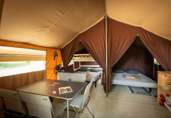 Interior view of a classic safari tent with dining table, chairs, and two sleeping areas at Huttopia Lac d'Aureilhan.