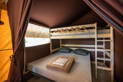 Intérieur d'une tente safari confortable avec lit double et lit superposé au Huttopia Lac d'Aureilhan, Mimizan.