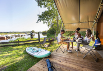 Tres personas desayunan en la terraza de una tienda safari en Huttopia Lac d'Aureilhan, junto al lago, en Francia.