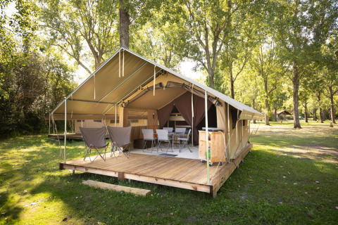 Klassisk safaritelte ved Huttopia Lac d'Aureilhan i Frankrig, omgivet af træer og grønne områder.