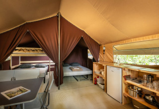 Interior of a safari tent suite with double bed, bunk beds, kitchenette, and dining area at Lac d'Aureilhan.