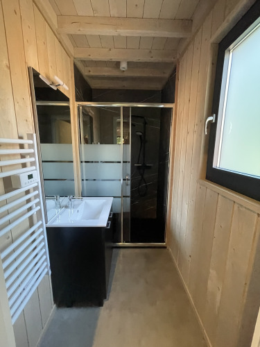 Moderne badkamer met houtafwerking, douche en lavabo in een Ecolodge tiny house in Hameau de l'Ourthe, België.