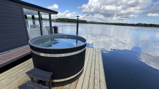 Uitzicht vanaf Houseboat Marina Mookerplas met een hottub op het dek aan het meer onder blauwe lucht.