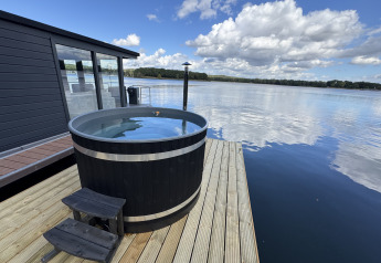 Blick von Houseboat Marina Mookerplas mit Hot Tub auf der Terrasse am See unter blauem Himmel.