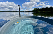 Blick auf einen idyllischen See von einer luxuriösen Glamping-Unterkunft mit einem runden Whirlpool draußen.