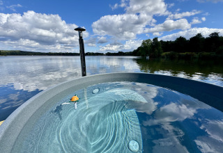 Uitzicht over een rustige plas vanaf een luxe glamping-accommodatie met een rond bubbelbad buiten.