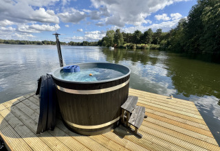 Bañera de hidromasaje junto al lago en una terraza de madera, rodeada de naturaleza y árboles.