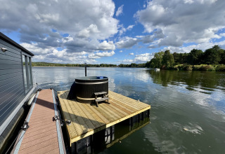Casa flotante en Marina Mookerplas, Países Bajos, con jacuzzi sobre una terraza de madera en el lago.
