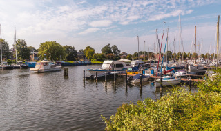 Boten en jachten in een haven, omringd door groen en huizen nabij Andijk, Noord-Holland, Nederland.