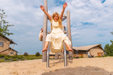 A joyful girl in a light dress slides down a playground slide at Vakantiepark IJsselhof holiday park.