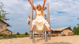 Blij meisje in lichte jurk glijdt van speeltuin glijbaan in Vakantiepark IJsselhof, Noord-Holland.