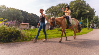 Vrouw begeleidt een pony met kind in Vakantiepark IJsselhof, populair vakantiepark in Noord-Holland.