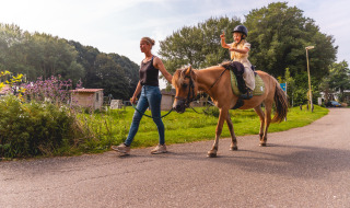 Vrouw begeleidt een pony met kind in Vakantiepark IJsselhof, populair vakantiepark in Noord-Holland.