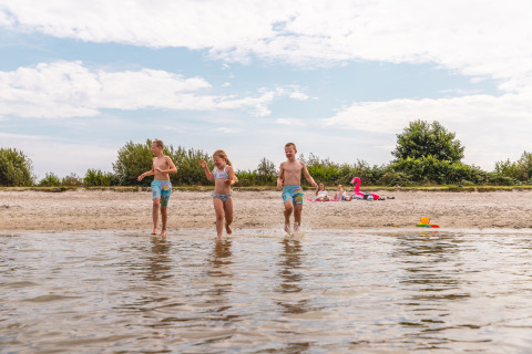 Drie kinderen spelen aan het water op een strand vlakbij Andijk, Nederland, tijdens een zonnige dag.