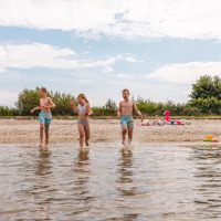 Drie kinderen spelen aan het water op een strand vlakbij Andijk, Nederland, tijdens een zonnige dag.