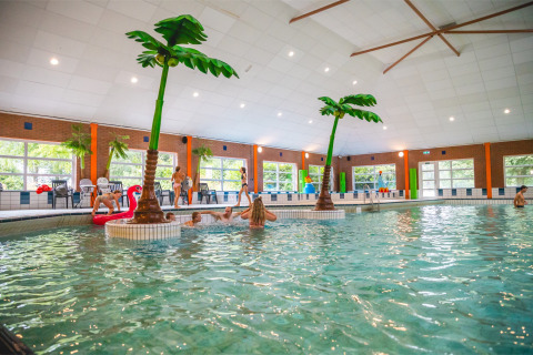 Indoor swimming pool with artificial palm trees and people swimming at Vakantiepark IJsselhof, North-Holland.