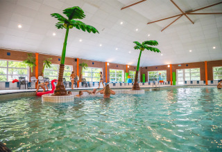 Piscina cubierta con palmeras artificiales y bañistas en Vakantiepark IJsselhof, Holanda Septentrional.
