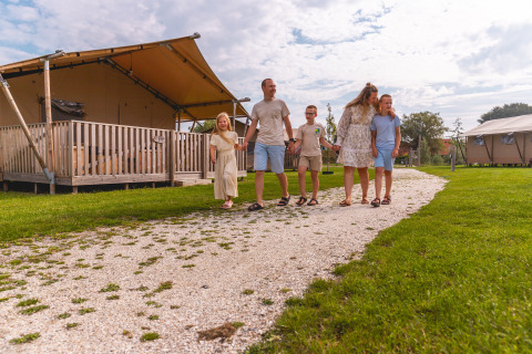 Famiglia che cammina su un sentiero vicino alle tende al Vakantiepark IJsselhof, parco vacanze in Olanda Nord.
