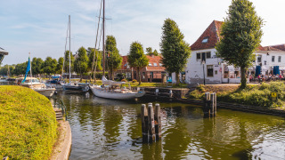 Boten aangemeerd aan een kanaal bij Vakantiepark IJsselhof, met bomen, huizen en terras in Noord-Holland.