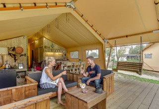 Stel geniet van een drankje in een glampingtent met houten meubels bij Sandberghe, Noord-Brabant.