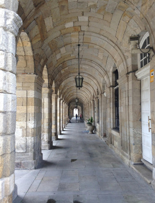 Galerie voûtée en pierre avec colonnes et lanternes à Prado, Lalín, Galice, Espagne. Deux personnes marchent.