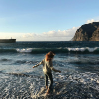 Une personne s’amuse dans les vagues sur la plage, montagnes et jetée en arrière-plan près de Prado, Galice.
