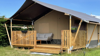 Tenda safari con veranda in legno e zona salotto accogliente, perfetta per glamping sotto cielo sereno.