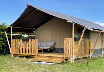 Safarizelt mit Holzveranda und Sitzbereich, ideal zum Glamping, aufgenommen bei sonnigem Wetter.