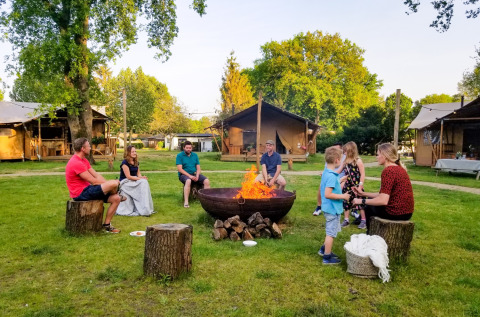 Gezellig samenzijn van gezinnen rond een kampvuur met safaritenten bij vakantiepark Sandberghe.