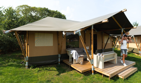 Famiglia davanti a una tenda safari di lusso, Safaritent Medley, con veranda e arredi moderni immersi nel verde.
